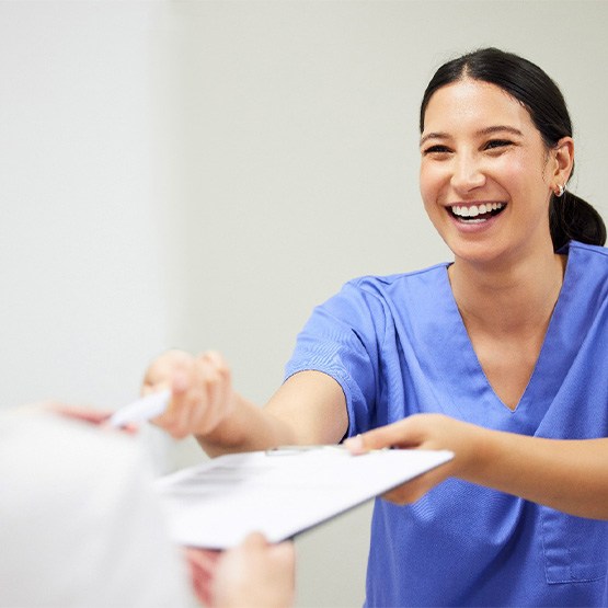 Dental assistant smiling while handing patient form