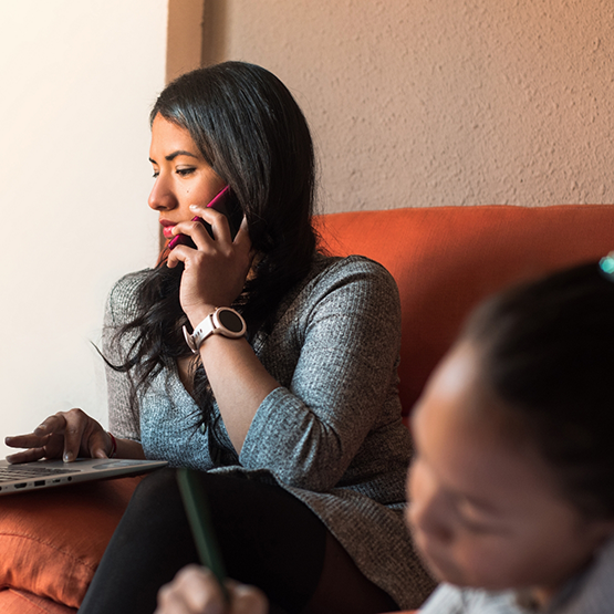 Woman sitting on couch and talking on the phone while using laptop