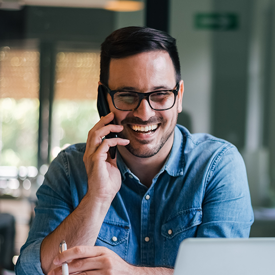 Man in denim shirt smiling while talking on phone