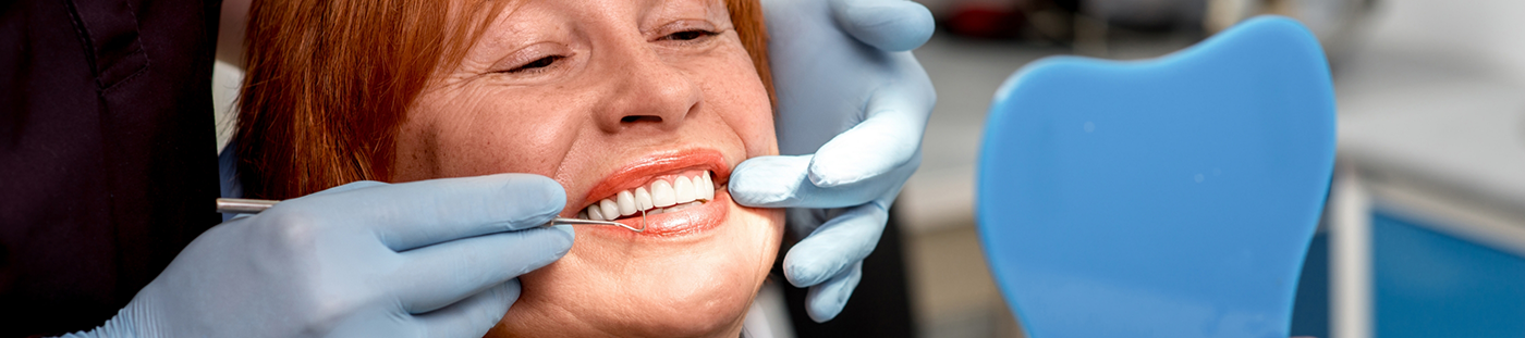 Woman admiring her new smile in mirror with dental implants in Arleta