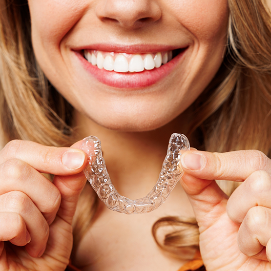 Smiling woman holding an Invisalign clear aligner