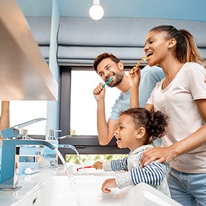 A man, woman, and little girl all brushing their teeth at the bathroom sink