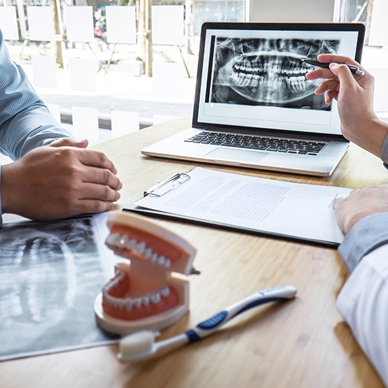 Dentist sitting at desk with patient and showing them dental x rays