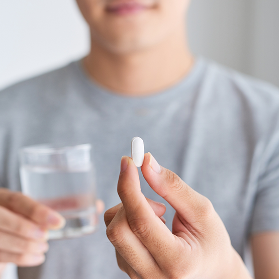 Person holding a white pill and a glass of water