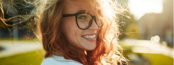 Redheaded woman with glasses smiling on a sunny day